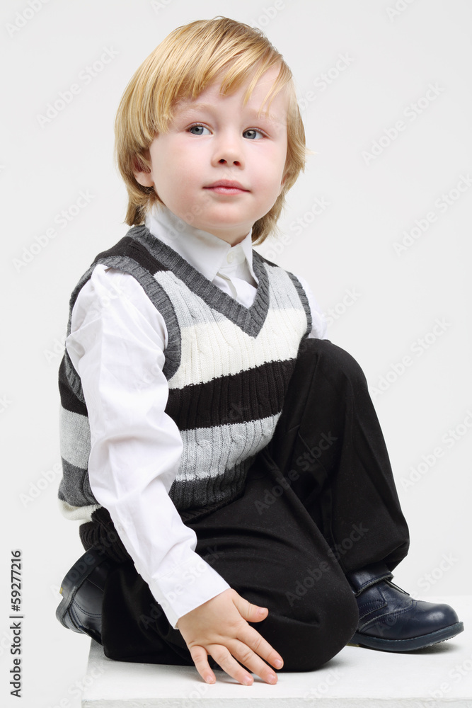 Little blond boy in vest sits and looks away on white background Little blond boy in vest sits and looks away on white background