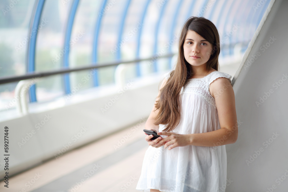 Pretty girl in white blouse with mobile phone looks at camera Pretty girl in white blouse with mobile phone looks at camera