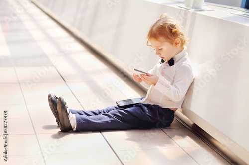 Red hair little cute girl sits on floor and holds cell phone