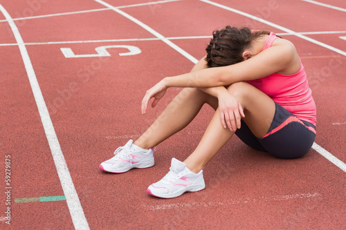 Tensed sporty woman sitting on the running track