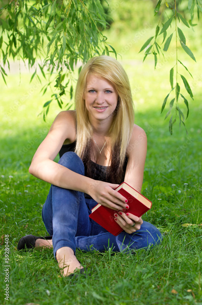 Schülerin mit Buch im Schatten eines Baumes