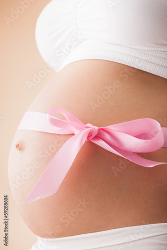 Pregnant belly with pink ribbon. Third trimester.