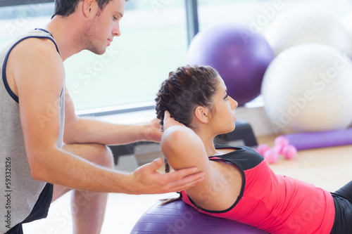 Male trainer helping woman do crunches on fitness ball at gym