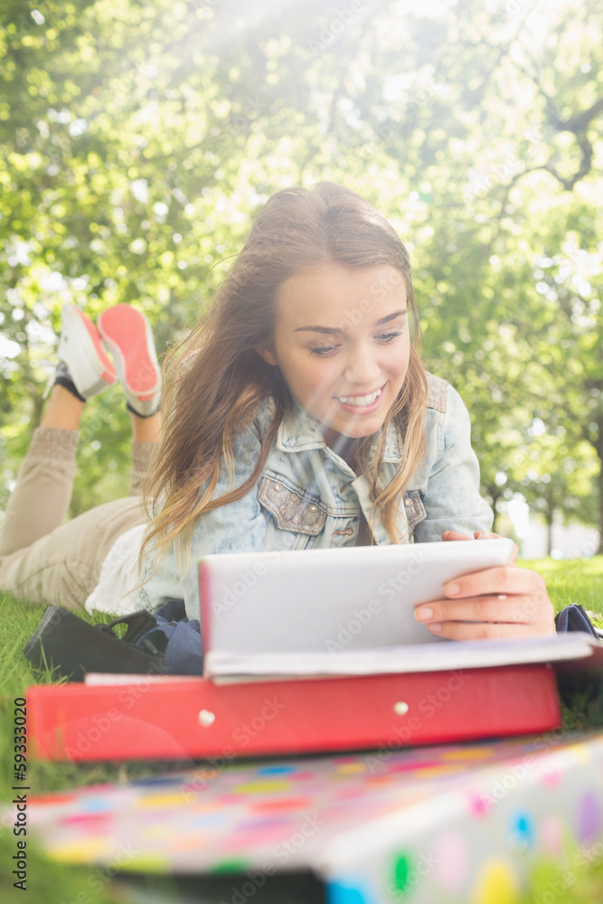 Pretty young student lying on the grass studying with her tablet Pretty young student lying on the grass studying with her tablet