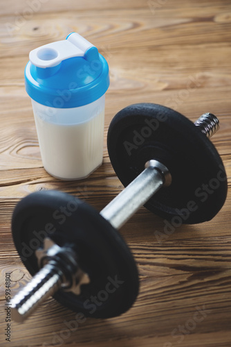 Dumbbell and protein drink on a wooden surface, vertical shot