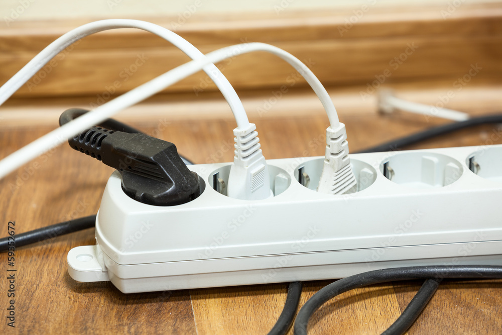 Many plugs plugged into electric power bar on office floor Many plugs plugged into electric power bar on office floor