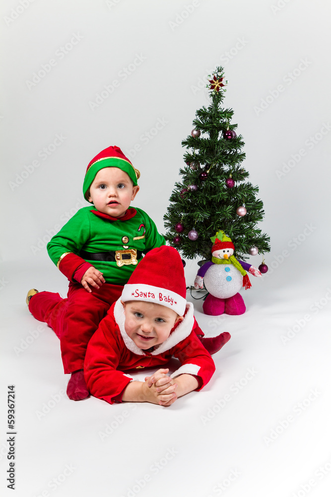 Two baby boys dressed as Santa Claus and Santa's Helper lying ne - obrazy, fototapety, plakaty 