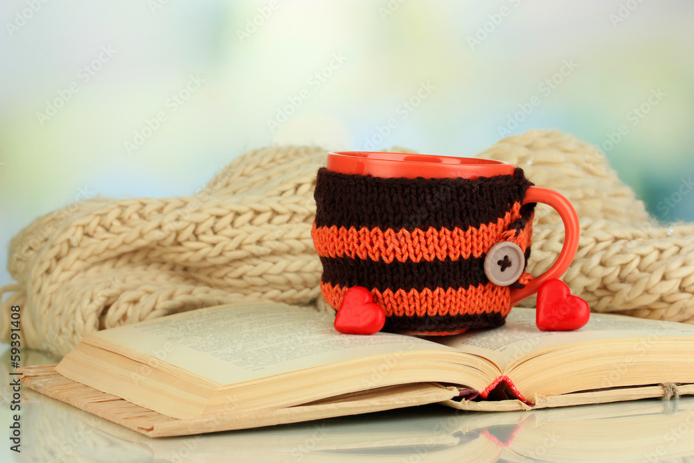 Fototapeta premium Cup with knitted thing on it and open book close up