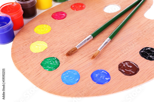Wooden art palette with paint and brushes close-up