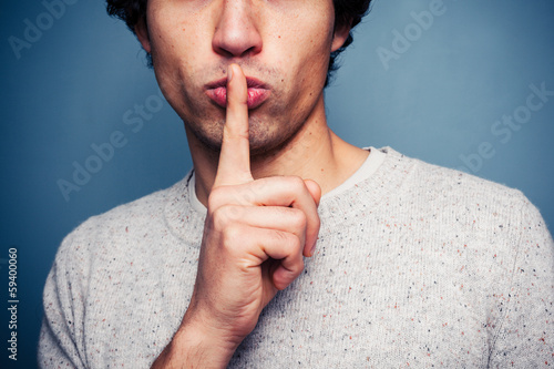Young man gesturing hush with finger on lips photo