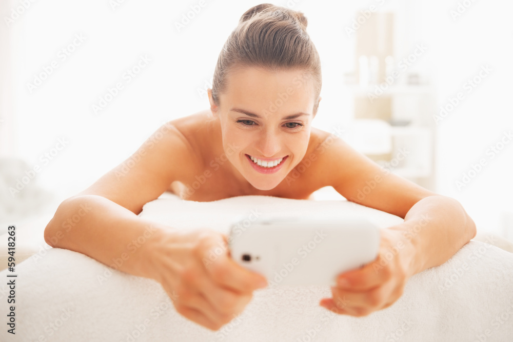 Happy woman writing sms while laying on massage table Happy woman writing sms while laying on massage table