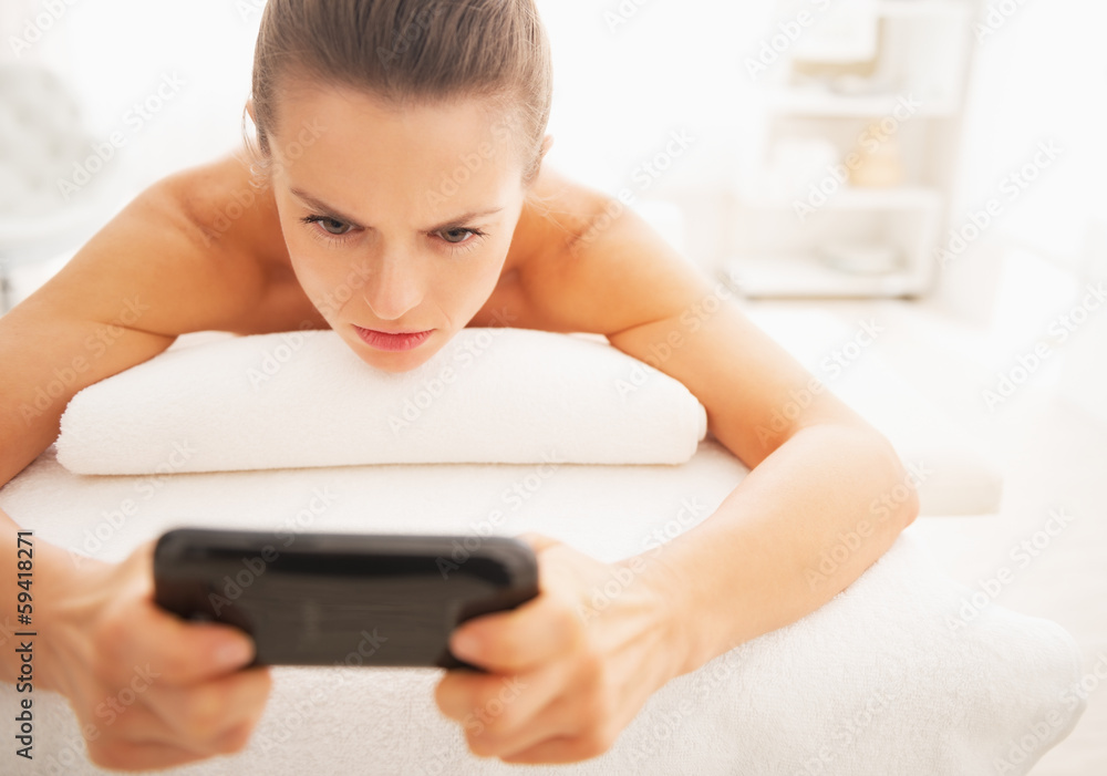 Concerned young woman reading sms while laying on massage table Concerned young woman reading sms while laying on massage table