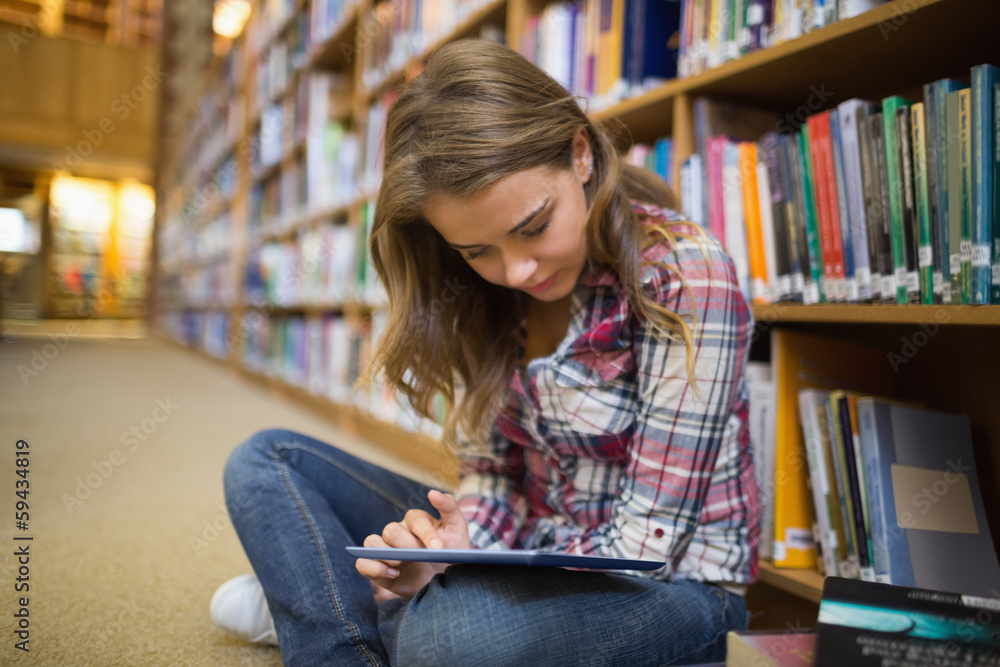 Pretty student sitting on library floor using tablet Pretty student sitting on library floor using tablet