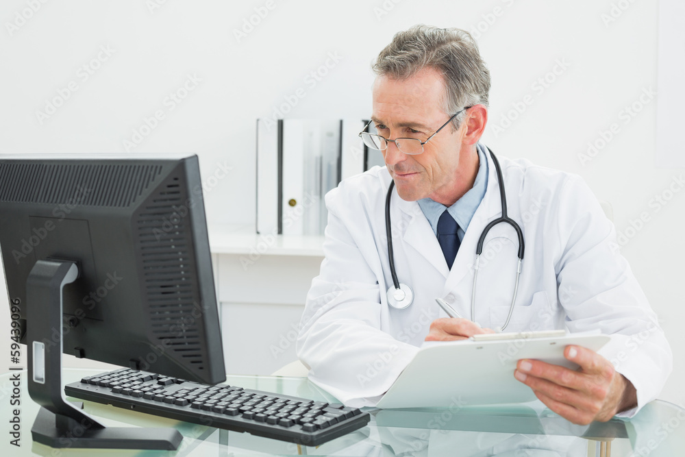 Doctor with report looking at computer monitor at medical office Doctor with report looking at computer monitor at medical office