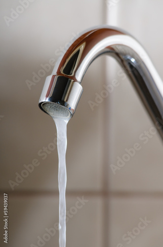 Vertical image of a tap with water flowing slowly during a period of scarcity