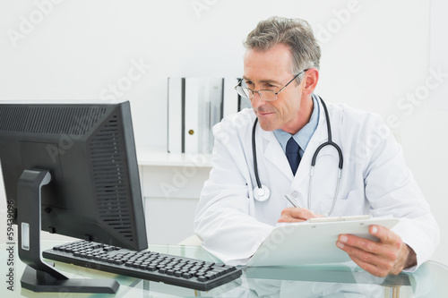 Doctor with report looking at computer monitor at medical office