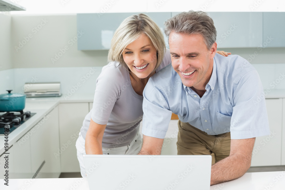 Happy couple using laptop in kitchen Happy couple using laptop in kitchen