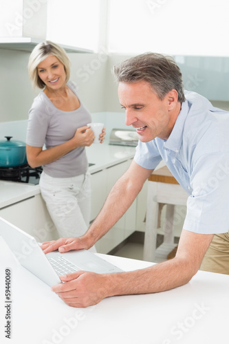 Man using laptop with woman in the kitchen