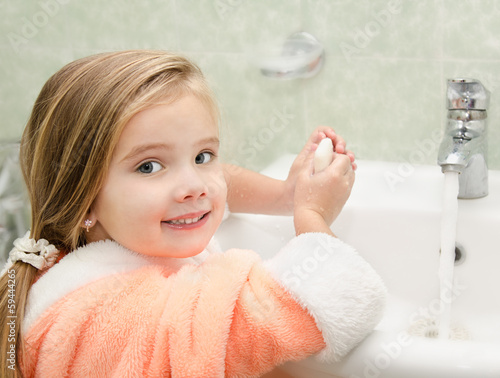 Smiling little girl washing hands in bathroom