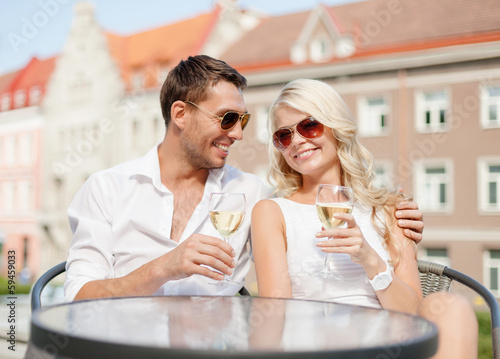 smiling couple in sunglasses drinking wine in cafe