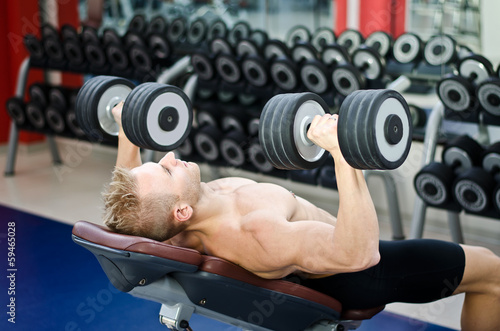 Muscular young man shirtless, training pecs on gym bench