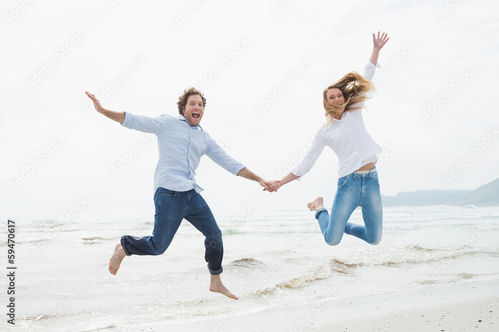 Cheerful couple holding hands and jumping at beach Cheerful couple holding hands and jumping at beach