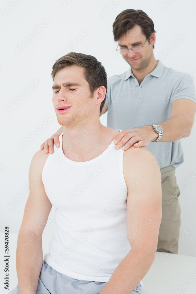Male physiotherapist massaging a young mans shoulder Male physiotherapist massaging a young mans shoulder