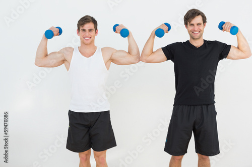 Portrait of two young men flexing muscles with dumbbells
