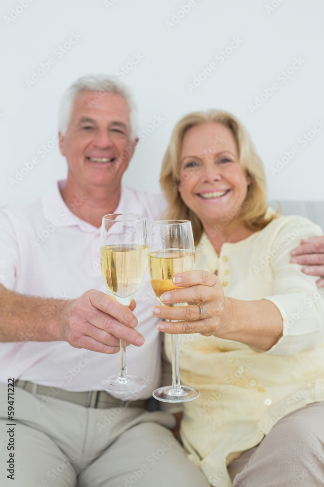 Senior couple holding out champagne flutes at home Senior couple holding out champagne flutes at home