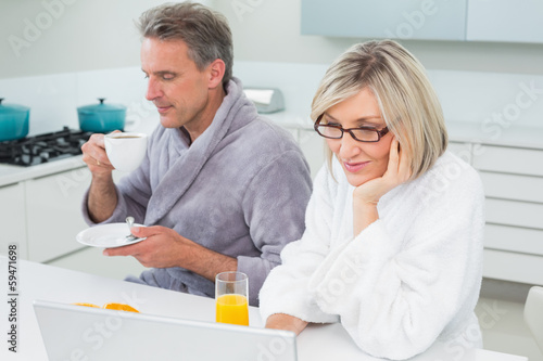 Couple in bathrobes with coffee and juice using laptop