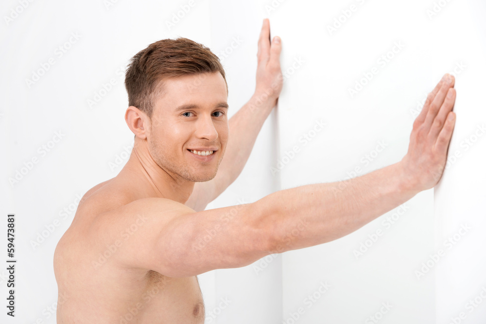 attractive nude guy resting both hands on a white wall. attractive nude guy resting both hands on a white wall.