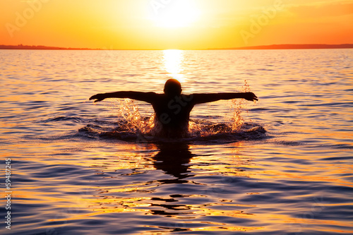 young man swims in the sea over sunrise