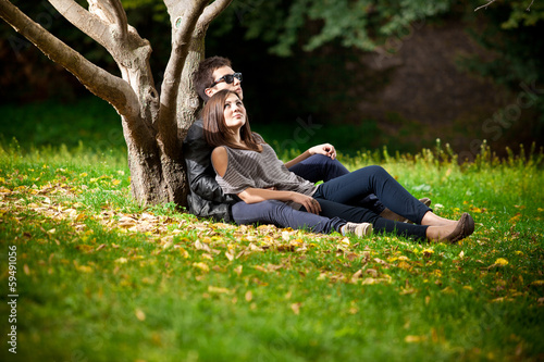 Young dating couple lying under tree in park and hugging