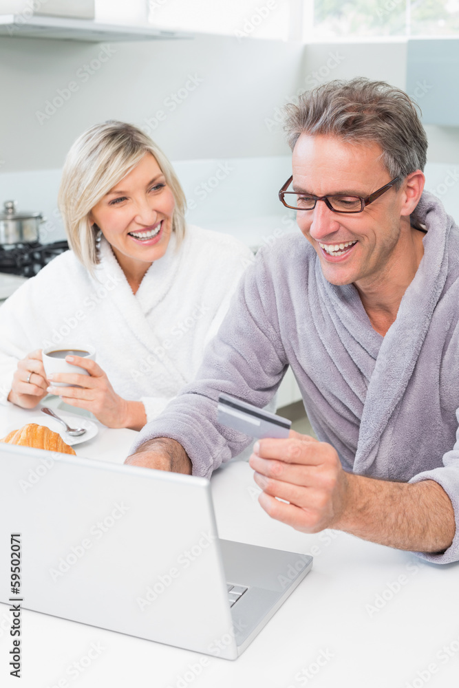 Couple in bathrobes using laptop in kitchen Couple in bathrobes using laptop in kitchen