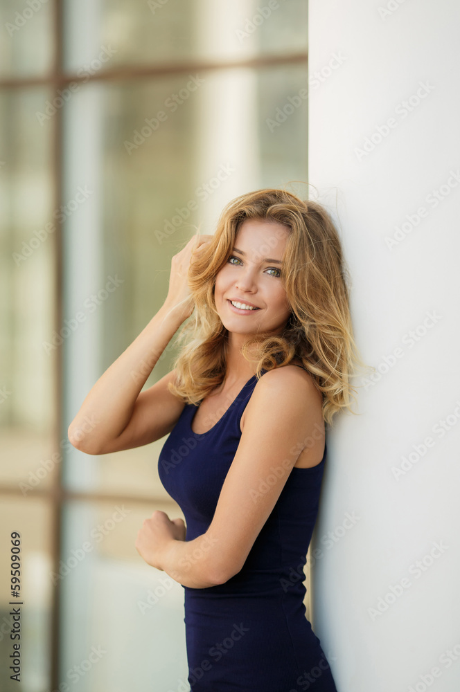Beautiful blonde woman standing by a stone wall on a summer day