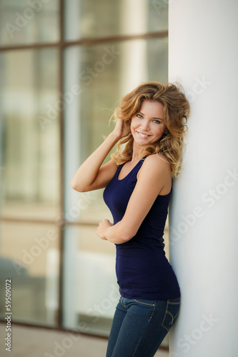 Beautiful blonde woman standing by a stone wall on a summer day