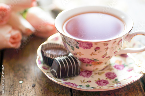 Close up of a cup of tea with roses and chocolate candies on woo