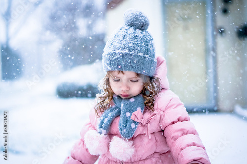 Cute baby girl in pink jacket and grey hat enjoying first snow b