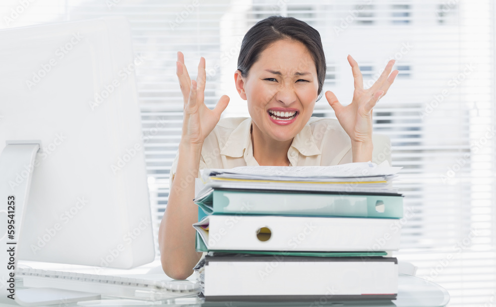 Angry businesswoman shouting with stack of folders at desk Angry businesswoman shouting with stack of folders at desk
