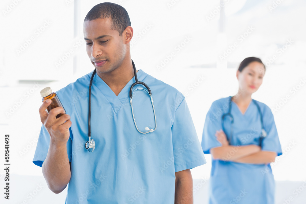 Doctor holding a bottle of pills with colleague in background Doctor holding a bottle of pills with colleague in background