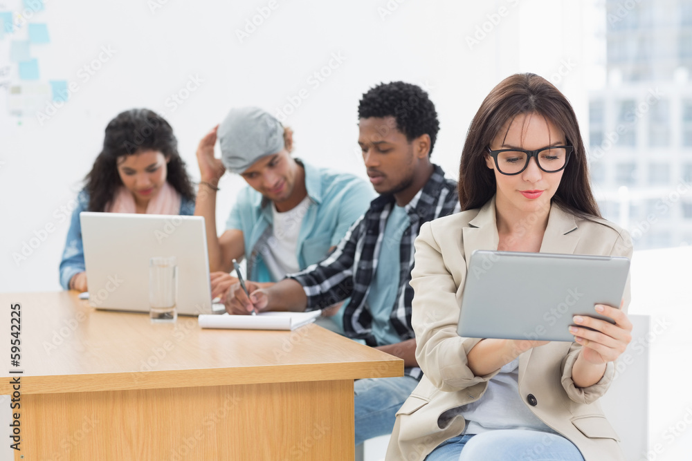 Concentrated woman using digital tablet with colleagues behind i Concentrated woman using digital tablet with colleagues behind i