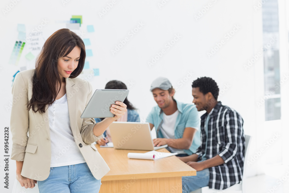 Woman using digital tablet with colleagues behind in office Woman using digital tablet with colleagues behind in office