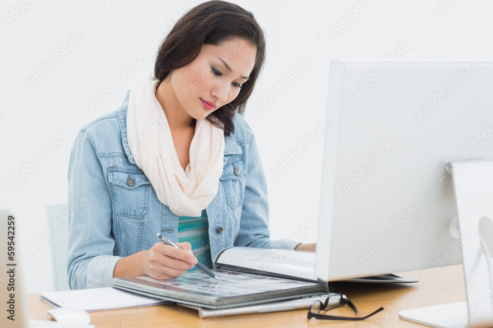 Woman looking at catalog in front of computer in office Woman looking at catalog in front of computer in office