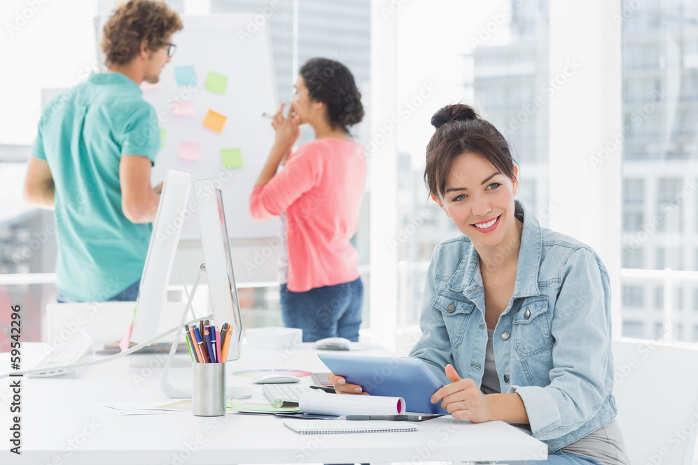Casual woman using digital tablet with colleagues behind in offi Casual woman using digital tablet with colleagues behind in offi