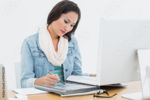 Woman looking at catalog in front of computer in office