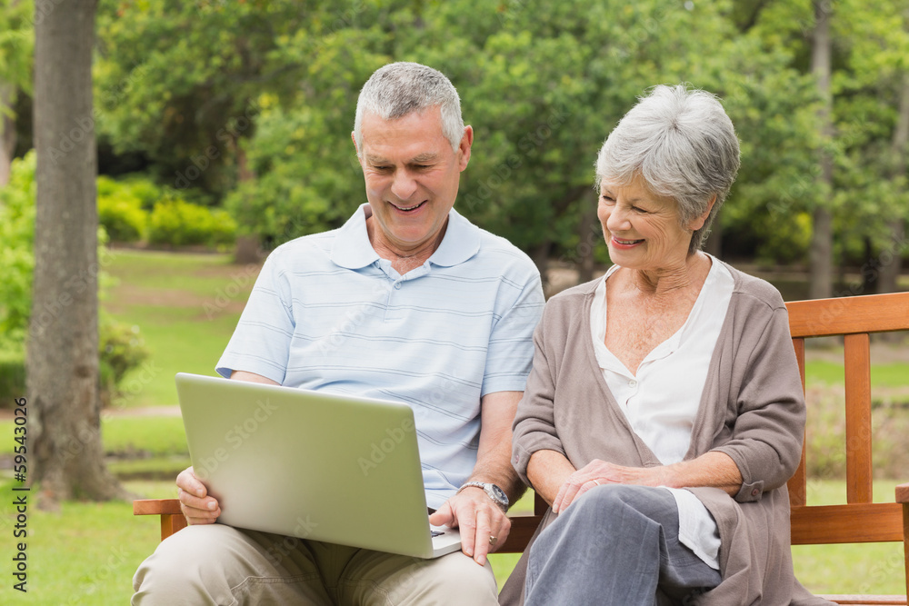 Smiling senior couple using laptop at park Smiling senior couple using laptop at park