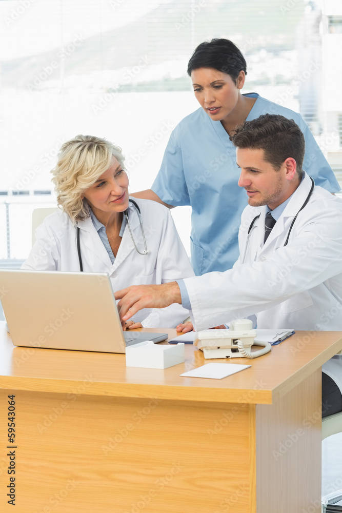Doctors using laptop together at the medical office Doctors using laptop together at the medical office