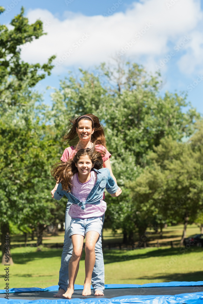 Fototapeta premium Happy girl and mother jumping high on trampoline in park