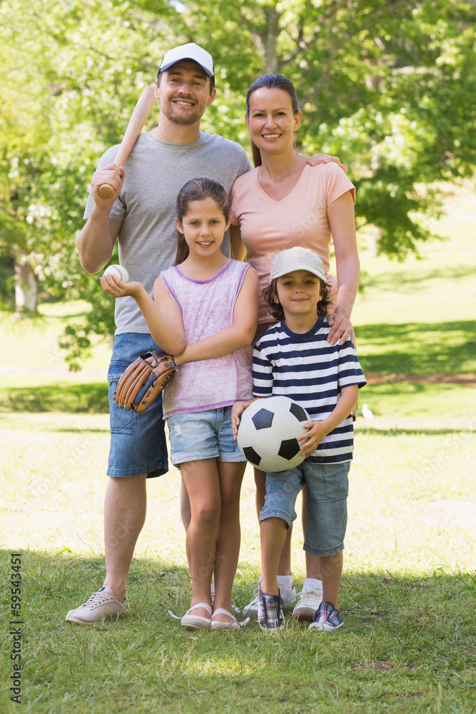 Family of four holding baseball bat and ball in park Family of four holding baseball bat and ball in park