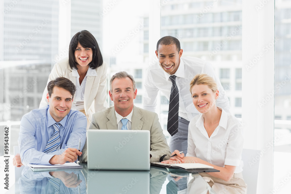 Happy business people gathered around laptop looking at camera